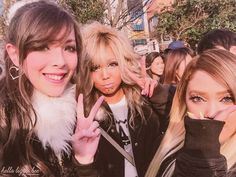 two women making the peace sign with their fingers in front of them and one woman holding her hand up