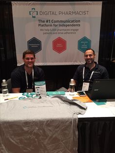 two men sitting at a table with laptops in front of them and a banner behind them