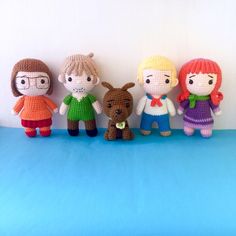 four crocheted dolls standing next to each other on top of a blue surface