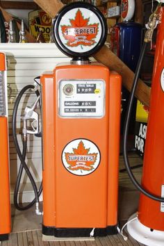 an orange gas pump sitting on top of a wooden floor next to two other pumps