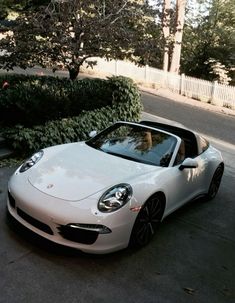 a white sports car is parked on the side of the road in front of some bushes