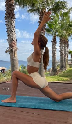 a woman is doing yoga on a mat near some palm trees and the ocean in the background