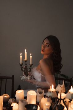 a woman sitting at a table with candles in front of her and looking into the distance