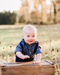 a smiling baby sitting on top of a wooden crate in the middle of a field