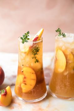 two glasses filled with drinks sitting on top of a table next to peaches and other fruit