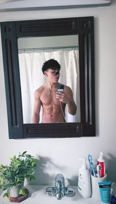 a man with no shirt is taking a selfie in front of a bathroom mirror