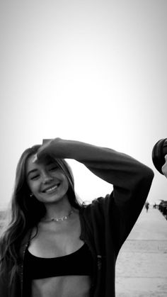 a woman standing on the beach with her arms behind her head and smiling at the camera