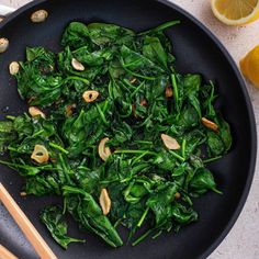 spinach and almonds cooking in a wok with chopsticks on the side