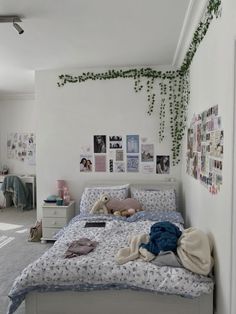 an unmade bed in a white bedroom with pictures on the wall and plants growing over it