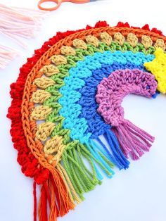 there is a crochet rainbow on the table next to some scissors and yarn