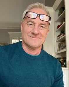 a man with glasses is smiling at the camera in front of a bookcase and bookshelves