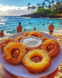 a person holding a plate with donuts and dip on it in front of the ocean