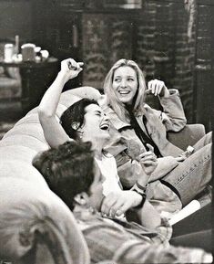 black and white photograph of two people laughing on a couch with one man holding his arm up in the air