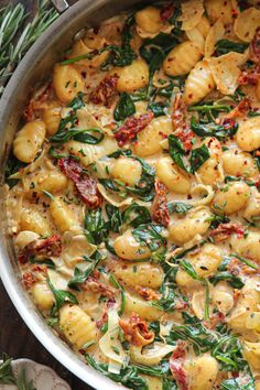 a pot filled with pasta and spinach covered in sauce on top of a wooden table