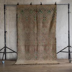 an old rug hanging on a tripod in front of a wall