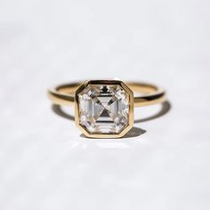 A solitaire asscher moissanite sits in a floating bezel-setting on this classically raised profile golden ring. The cut corners of the asscher provides for an octagonal silhouette, symbolic to serenity. Every millimeter of this ring has been carefully thought out by our experienced designers and artisans. Suitably accompanying the chic stone setting is a perfectly balanced 4-pillar inverted pyramid, carrying the moissanite to the most ideal position for complimenting the depth of the stone. This Modern Moissanite Rings In Asscher Cut, Modern Moissanite Asscher Cut Rings, Modern Moissanite Rings With Asscher Cut, Asscher Cut Diamond Ring With Single Cut Diamonds, Modern Asscher Cut Moissanite Rings, White Gold Asscher Cut Ring With Bezel Setting, White Gold Rings With Bezel Setting, Asscher Cut, Asscher Cut Diamond Ring With Bezel Setting, Formal Asscher Cut Ring With Bezel Setting