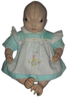 an old doll is wearing a blue dress and holding her hands in the air with one hand