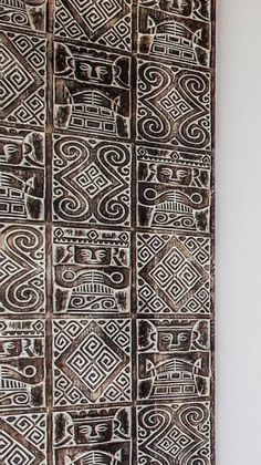 an intricately designed wall hanging on the side of a white wall with black and brown designs