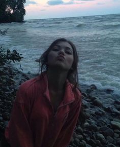 a woman standing next to the ocean with her eyes closed