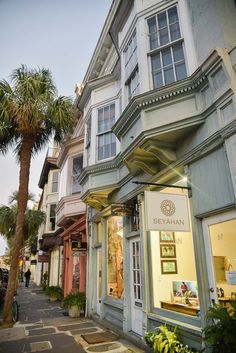 an old building with palm trees in front of it and people walking on the sidewalk