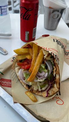 a sandwich with french fries and ketchup sits on a table next to a soda