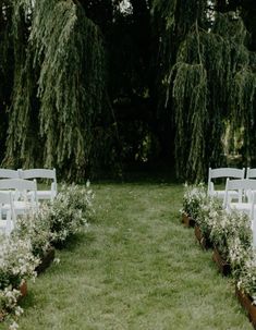 an outdoor ceremony setup with white chairs and flowers on the grass, surrounded by trees