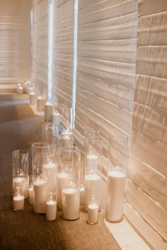 candles are lined up on the floor in front of a row of white glass vases