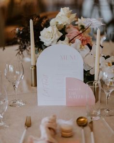 the table is set with white and pink flowers, candles, napkins and place settings