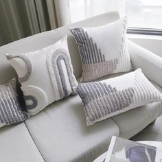 a white couch with two pillows on it next to a window and a book shelf