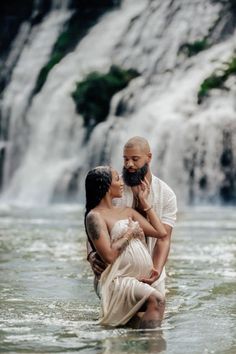 a man and woman standing in the water next to a waterfall, holding each other