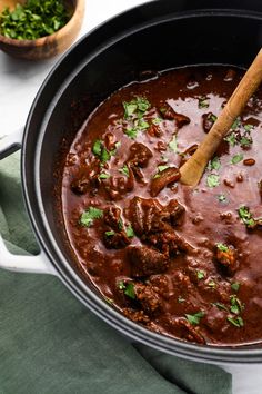 a pot filled with meat and garnish on top of a green napkin next to a wooden spoon