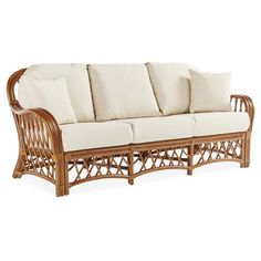 a wicker couch with white pillows on it's back and side cushions, in front of a white background