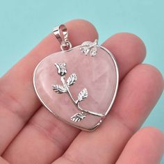 Genuine pink rose quartz is cut and polished into a heart shape and set in a silver tone metal open-back bezel with silver metal flower embellishments. Size: 32mm wide, 43mm long including bail Thickness: 10mm Bail: can hold a chain up to about 3-3.5mm thick Quantity: 1 pendant Nickel-free Pink Heart Cut Jewelry, Silver Flower-shaped Jewelry For Valentine's Day, Silver Heart-shaped Rose Quartz Jewelry, Silver Rose Quartz Heart Jewelry, Elegant Rose Quartz Heart Pendant Jewelry, Rose Quartz Heart Charm Jewelry For Valentine's Day, Valentine's Day Rose Quartz Jewelry With Heart Charm, Valentine's Day Rose Quartz Heart Charm Jewelry, Heart-shaped Rose Quartz Jewelry For Valentine's Day