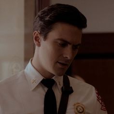 a man in uniform looking down at his cell phone while wearing a badge on his shirt and tie