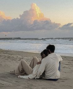 two people are sitting on the beach watching the sun go down and clouds in the sky