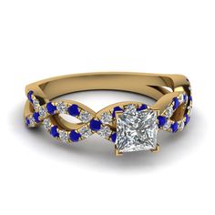 a princess cut diamond ring with blue stones on the band and side stones in 18k yellow gold