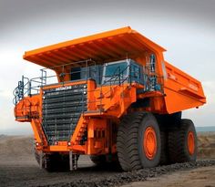 an orange dump truck parked on top of a dirt field