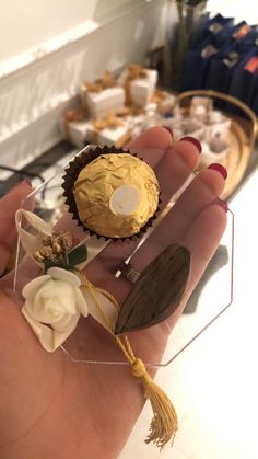 a hand holding some cupcakes with gold icing and flowers on them in front of a counter