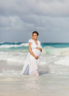 a pregnant woman standing in the ocean with her belly wrapped around her waist and wearing a white dress