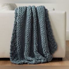 a blue knitted blanket sitting on top of a white couch next to a wooden floor