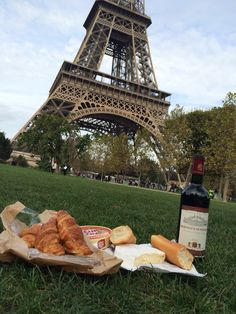 the eiffel tower is in the background with bread and wine on the grass