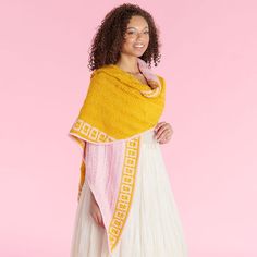 a woman wearing a yellow shawl and white dress standing in front of a pink background