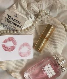 a bottle of perfume next to a note with lipstick imprints on it and pearls