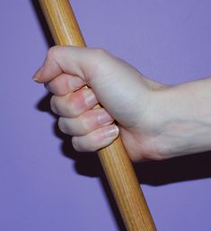 a person's hand holding onto a wooden stick against a purple background with the tip of their arm extended