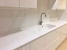 a kitchen with white cabinets and marble counter tops on each side, along with a stainless steel faucet