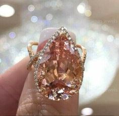 a woman's hand holding an orange and white diamond ring with diamonds around it