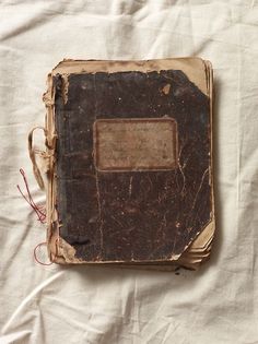 an old book sitting on top of a white cloth covered tablecloth with red string attached to it