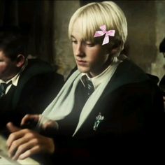 a woman with blonde hair sitting at a desk in front of two boys wearing school uniforms