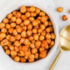 a white bowl filled with chickpeas next to a golden spoon on a white surface