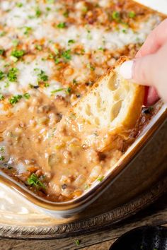 a hand dipping a piece of bread into a casserole dish